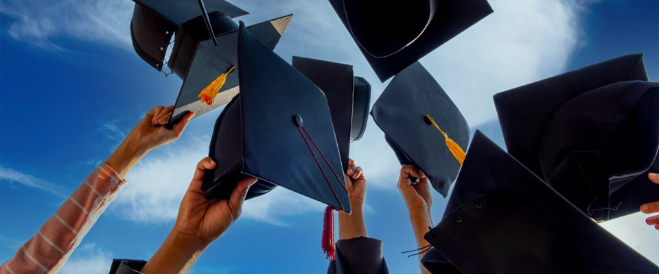 Κεντρική εικόνα για το θέμα: μεταπτυχιακό ή διδακτορικό. Χέρια φοιτητών σε κύκλο κρατούν τα καπέλα αποφοίτησής τους ψηλά.