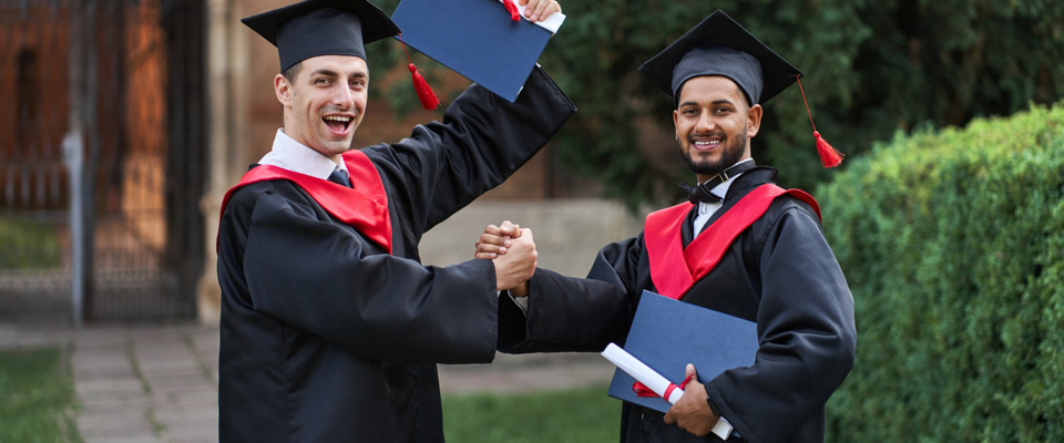 Δύο χαμογελαστοί φοιτητές συγχαίρουν ο ένας τον άλλον σε αποφοίτηση, έχοντας πάρει το μεταπτυχιακό ή διδακτορικό τους.