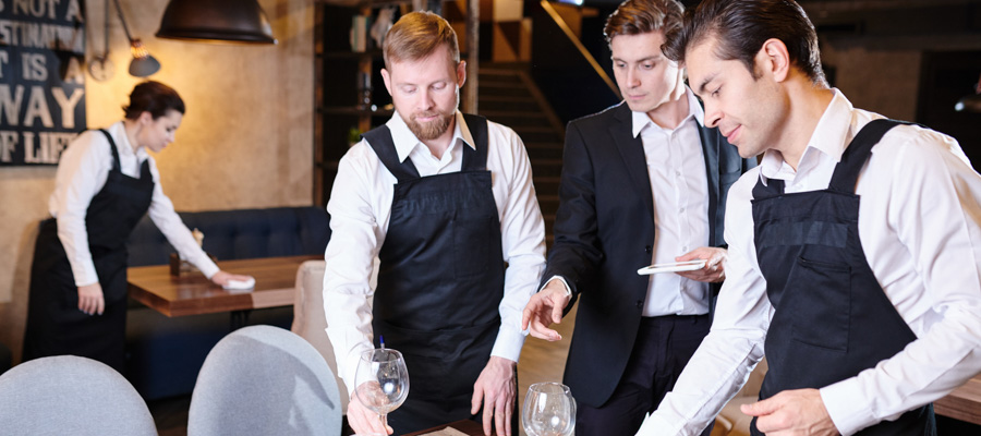 Food and Beverage manager δίνει οδηγίες σε δύο σερβιτόρους για το πώς να στρώσουν ένα τραπέζι εστιατορίου.