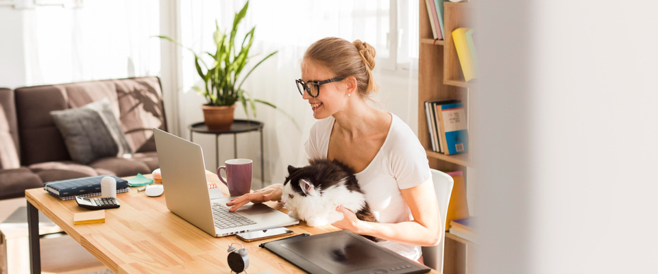 Χαμογελαστή κοπέλα με γυαλιά μυωπίας κάνει μεταπτυχιακές σπουδές από την άνεση του σπιτιού, έχοντας τη γάτα στα πόδια της.