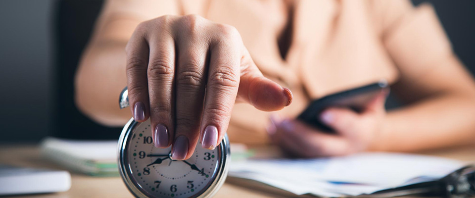 Γυναίκα κάνει σωστή διαχείριση χρόνου, κρατώντας ένα ρολόι με το χέρι της όσο δουλεύει.