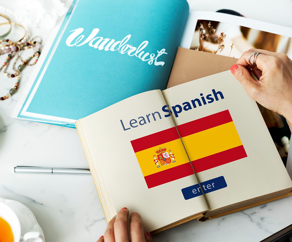 Γυναίκα κάνει ισπανικά για αρχάριους. Έχει ανοιχτό βιβλίο στο οποίο φαίνεται η ισπανική σημαία.