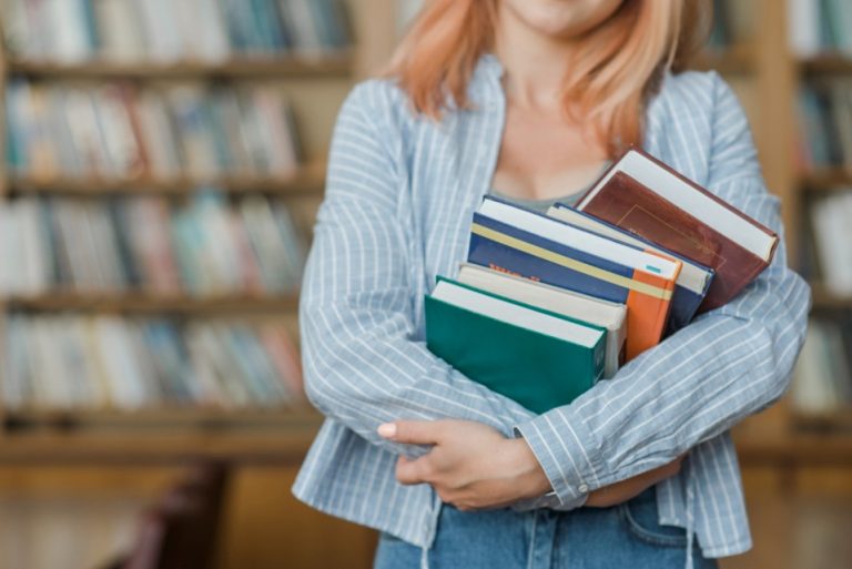 Θεματική εικόνα για πανεπιστήμιο ή ΙΕΚ. Φοιτήτρια κρατά στην αγκαλιά της πέντε βιβλία.
